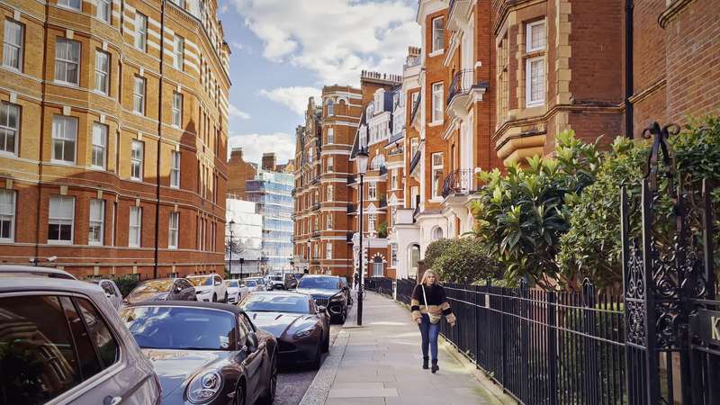 A quiet red-brick mansion-block street in west London in soft afternoon light.