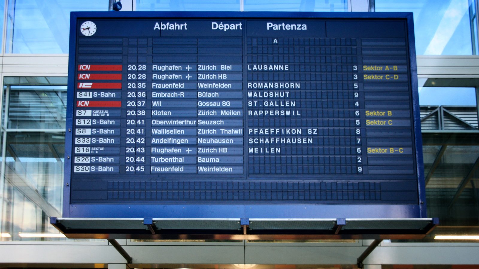 A large split-flap departure board at Winterthur station listing departure times, destinations and platform numbers, with a station clock below it.