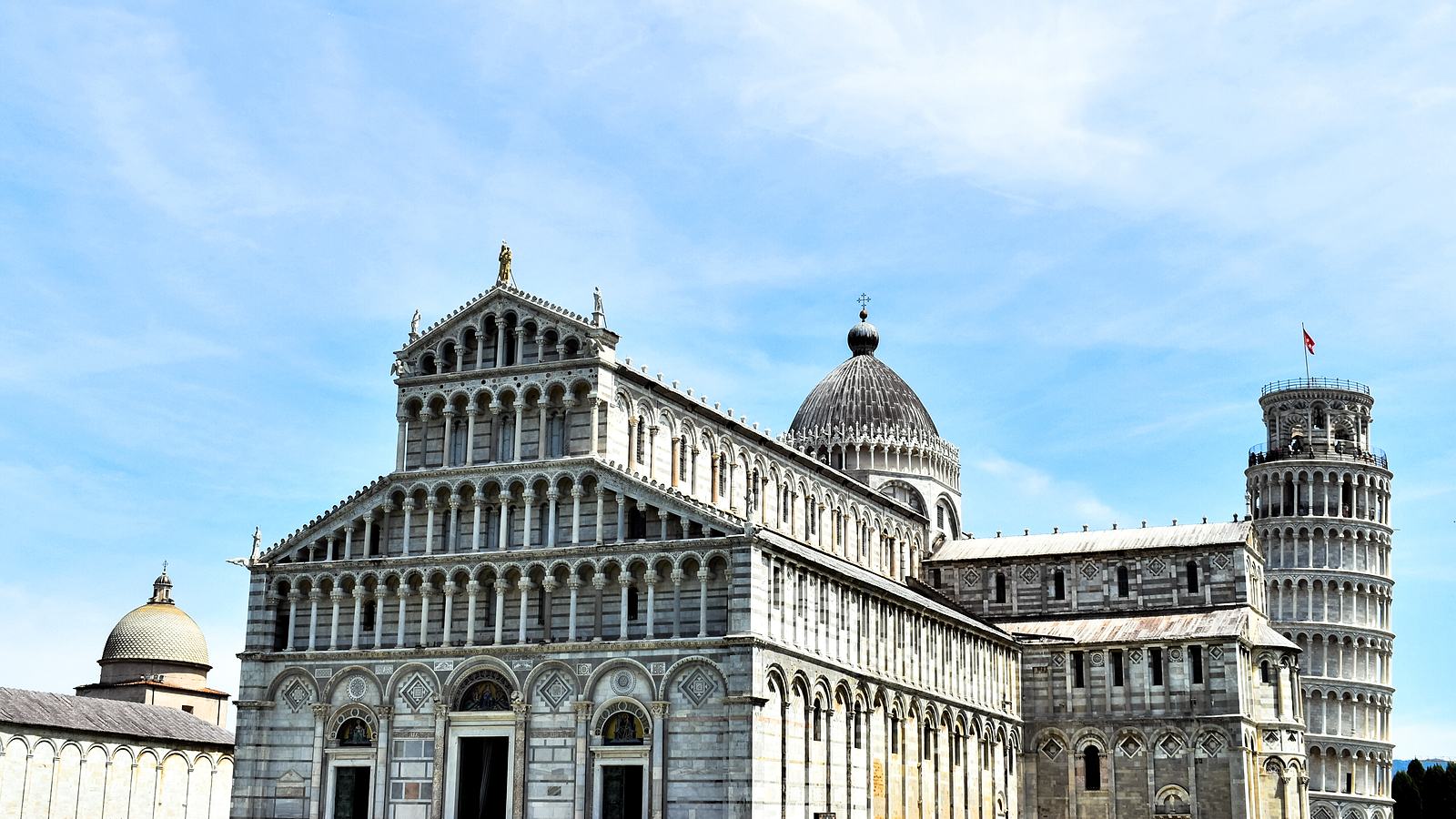 Pisa Cathedral and the leaning bell tower standing side by side on the Piazza dei Miracoli under a blue sky.