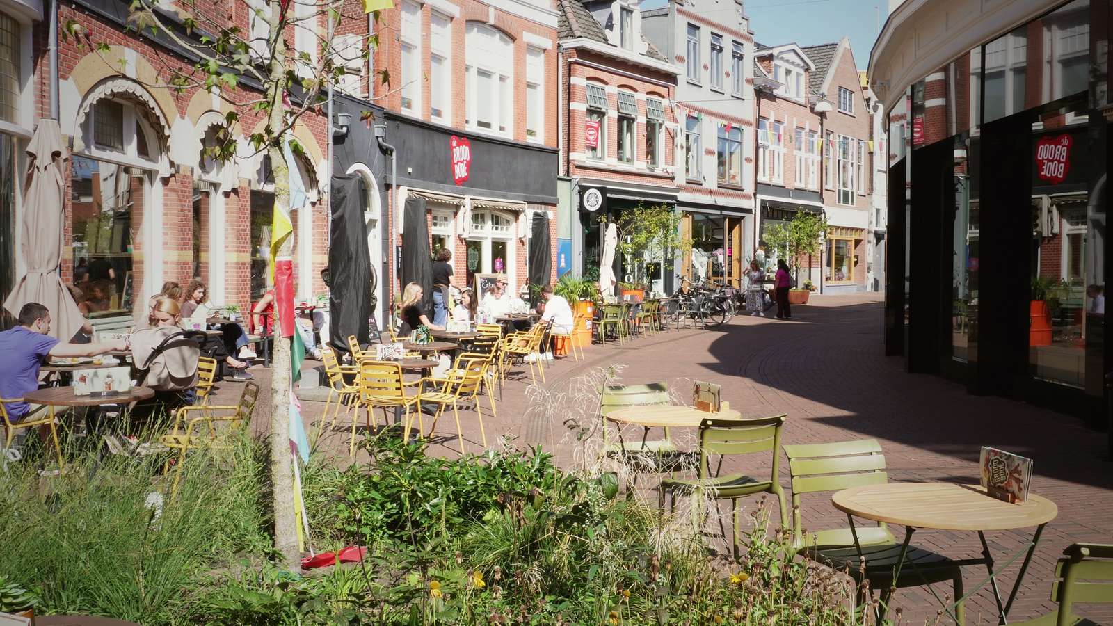 Café tables on a sunlit terrace in a Dutch old-town square.