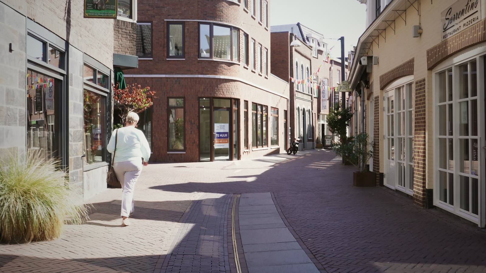 A traveller walking down a quiet, sunlit European lane.